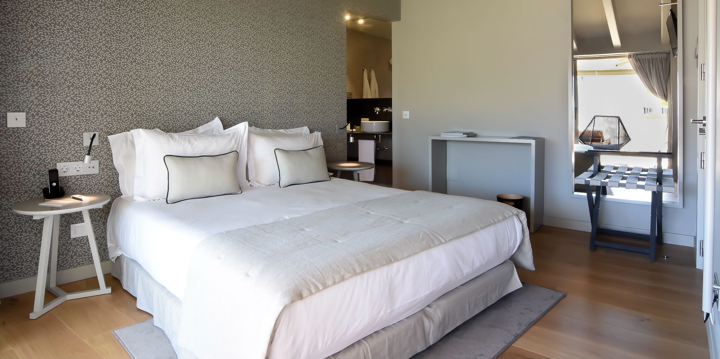Un dormitorio moderno con una cama grande, mesitas de noche, un escritorio y vistas al exterior.