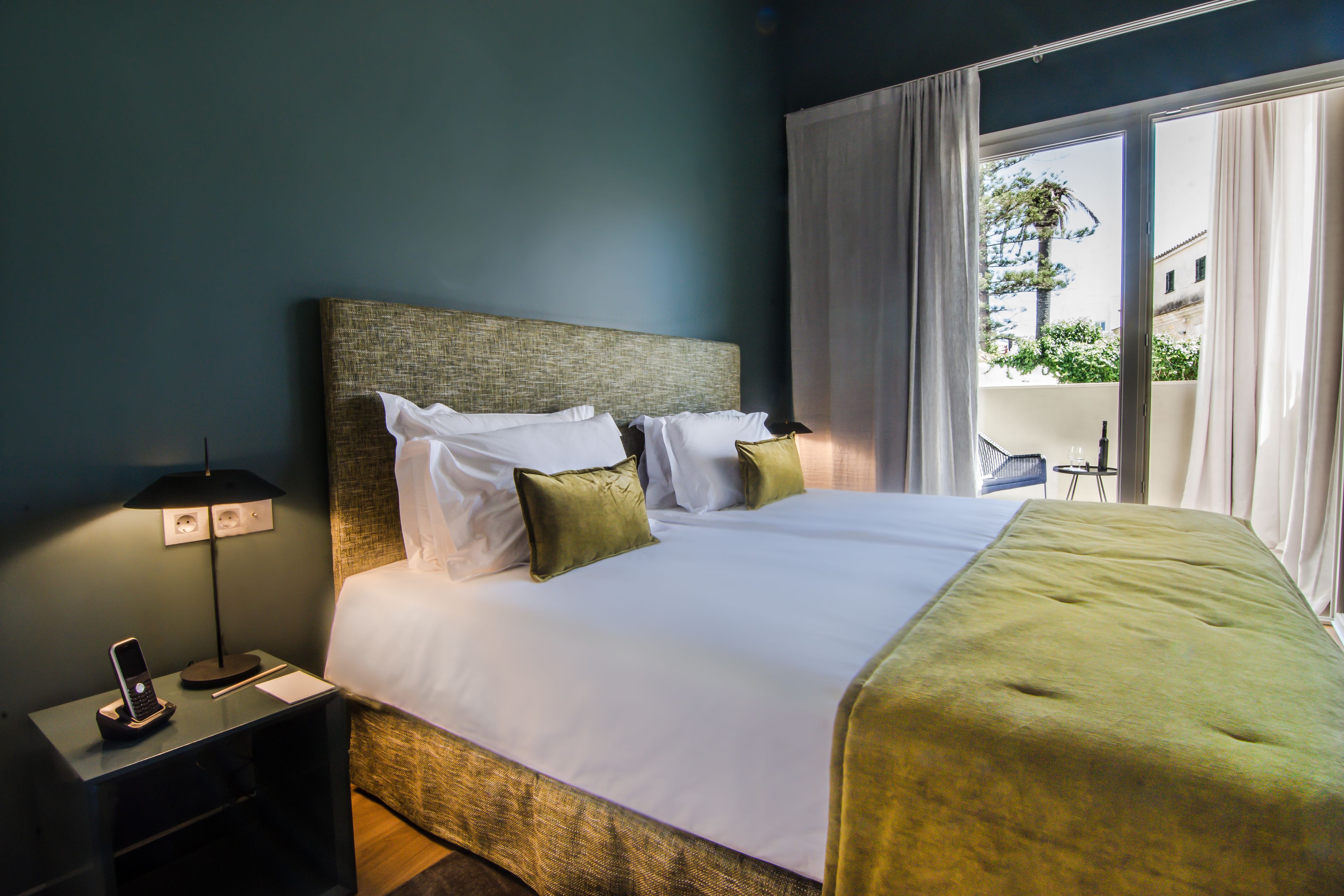 Une chambre d’hôtel avec un lit, une table de chevet avec un téléphone et une vue sur l’extérieur par une fenêtre.