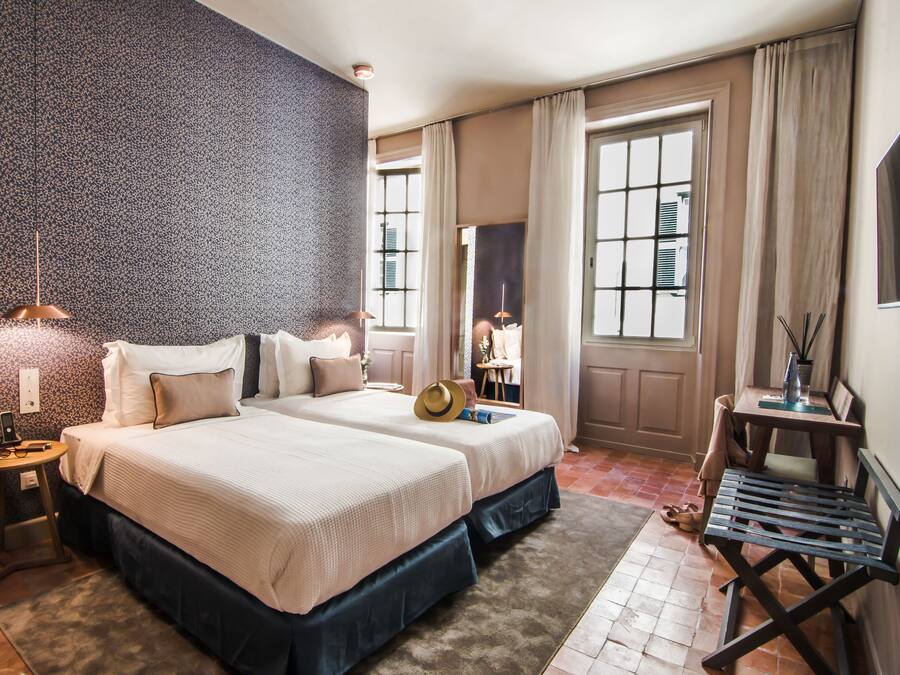 Habitación de hotel con dos camas, un escritorio, una silla, un televisor y un ventanal con cortinas.