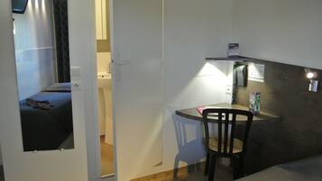 Une petite pièce comprenant un lit, un bureau avec une chaise, un téléphone et une lampe fixée au mur.