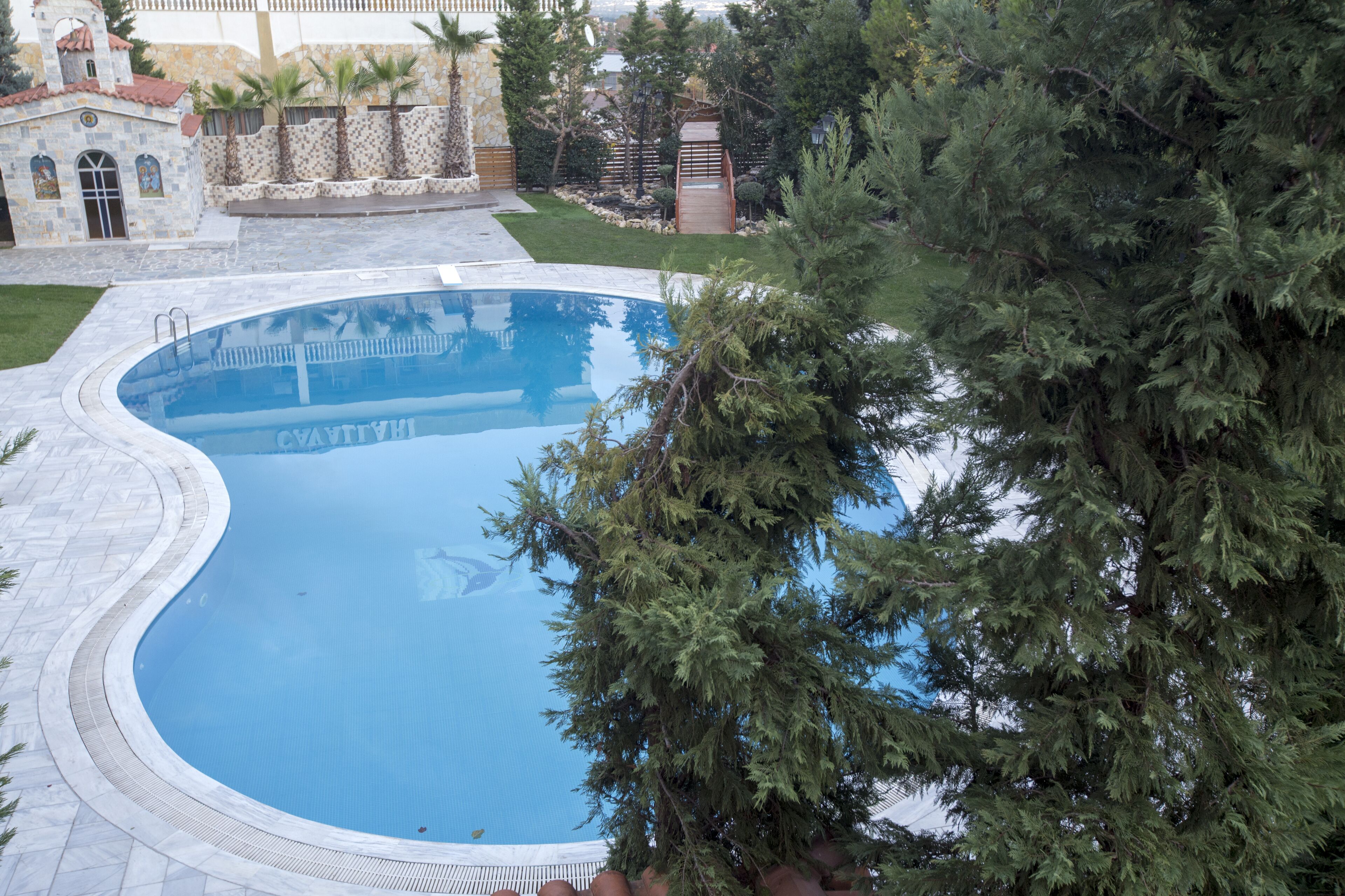 A large, curved swimming pool with a stone border, surrounded by a well-maintained lawn and trees.