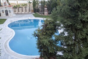 Una gran piscina curva con borde de piedra, rodeada por un césped bien cuidado y árboles.
