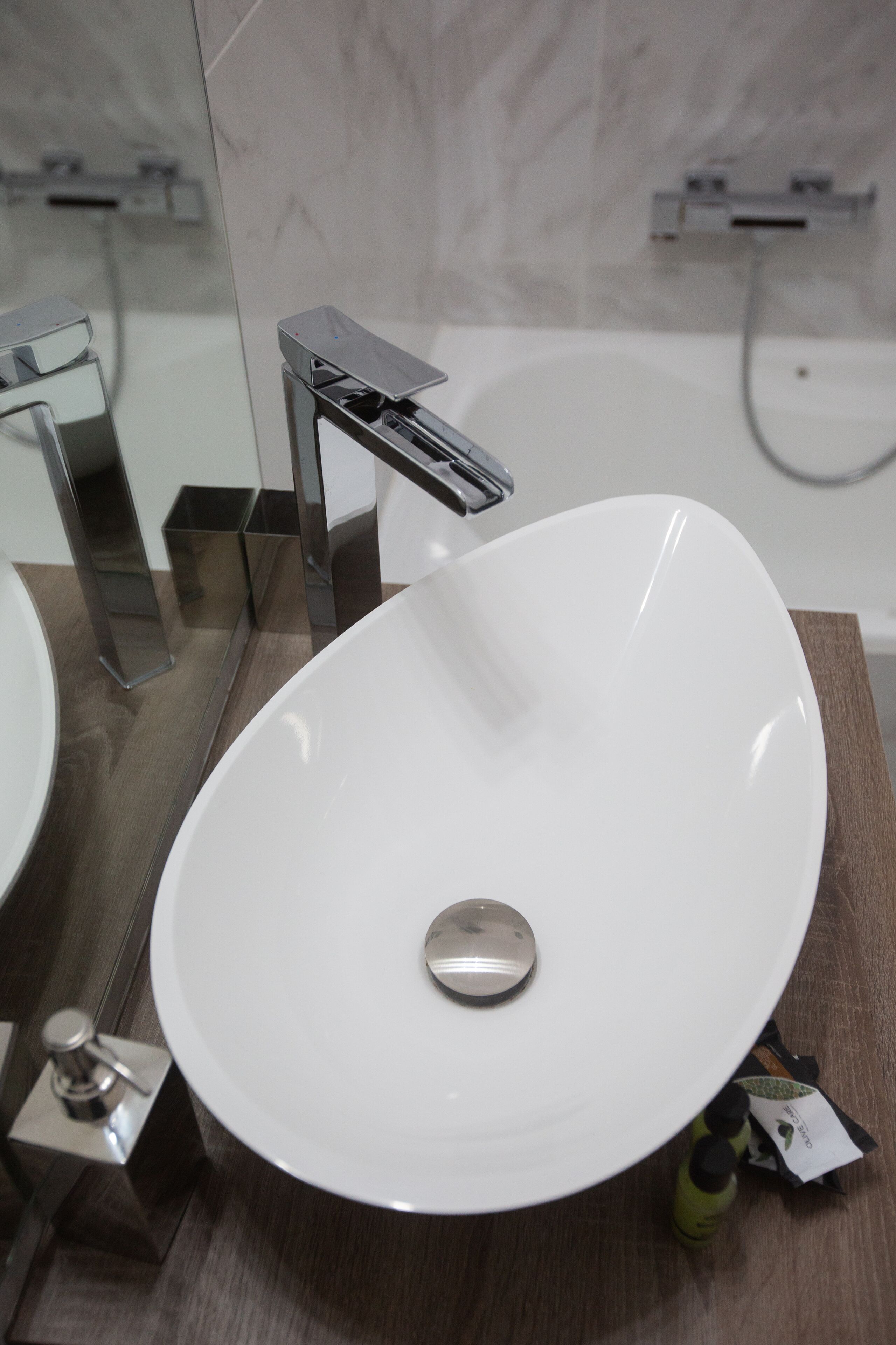 Un baño moderno con un lavamanos ovalado blanco, grifo cromado y un espejo encima.