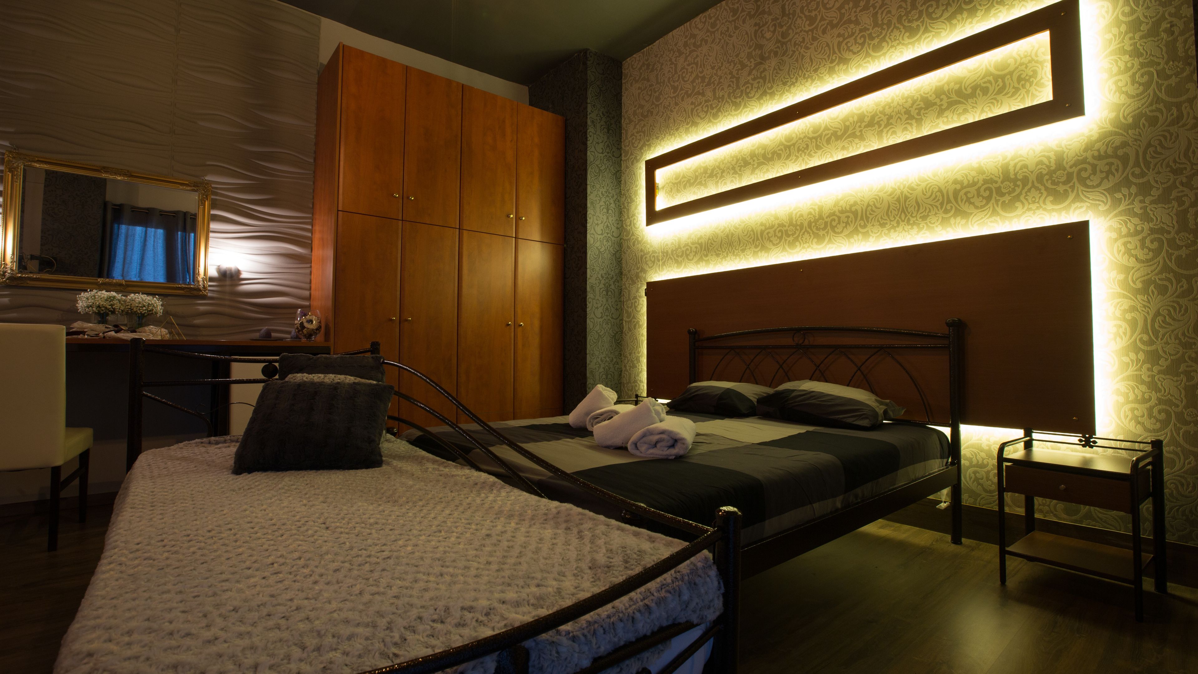 A modern bedroom with a bed, a wooden wardrobe, a desk, and a mirror.