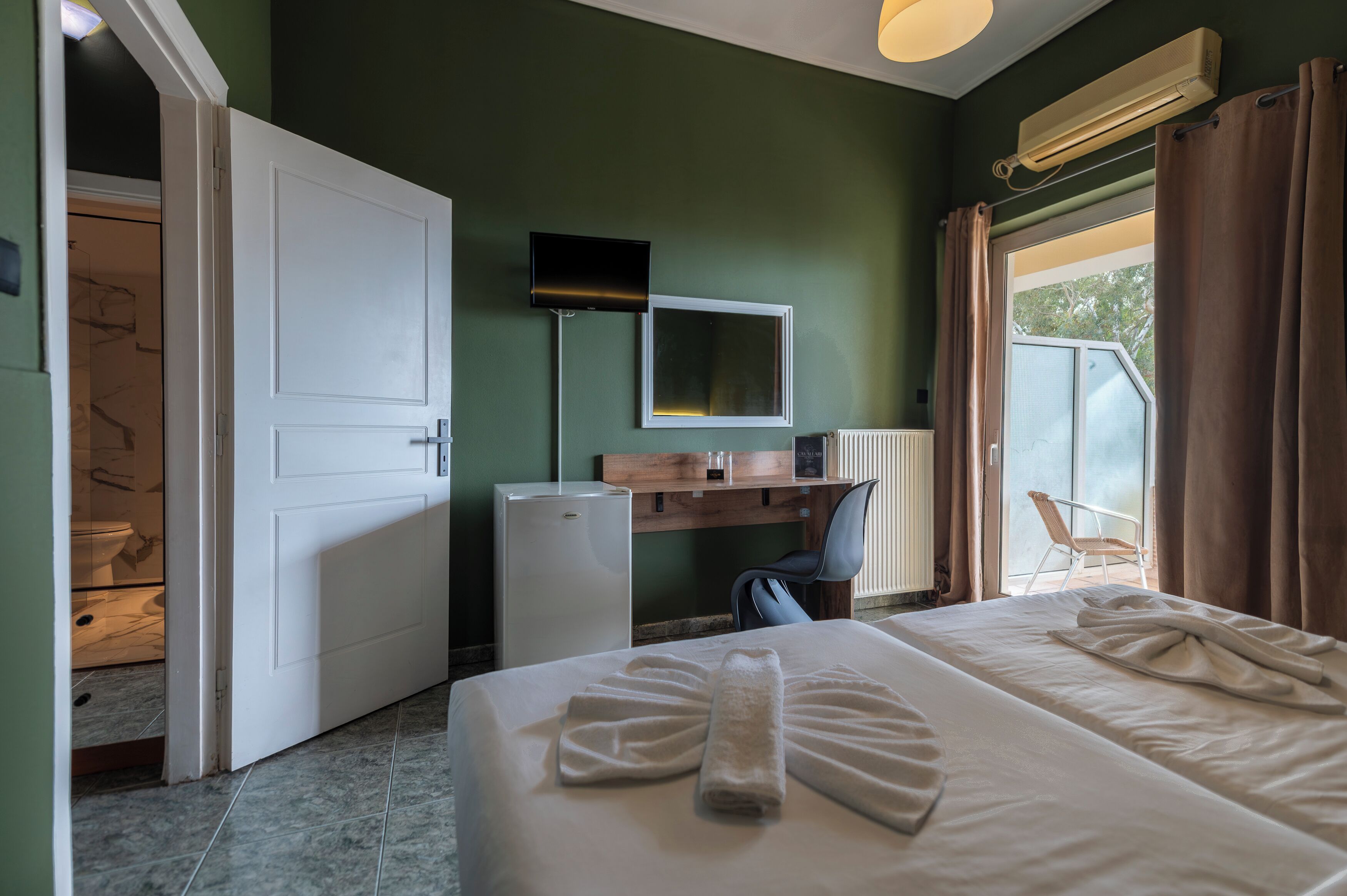 Una habitación de hotel con una cama, un escritorio, una silla, un televisor y una ventana con cortinas.