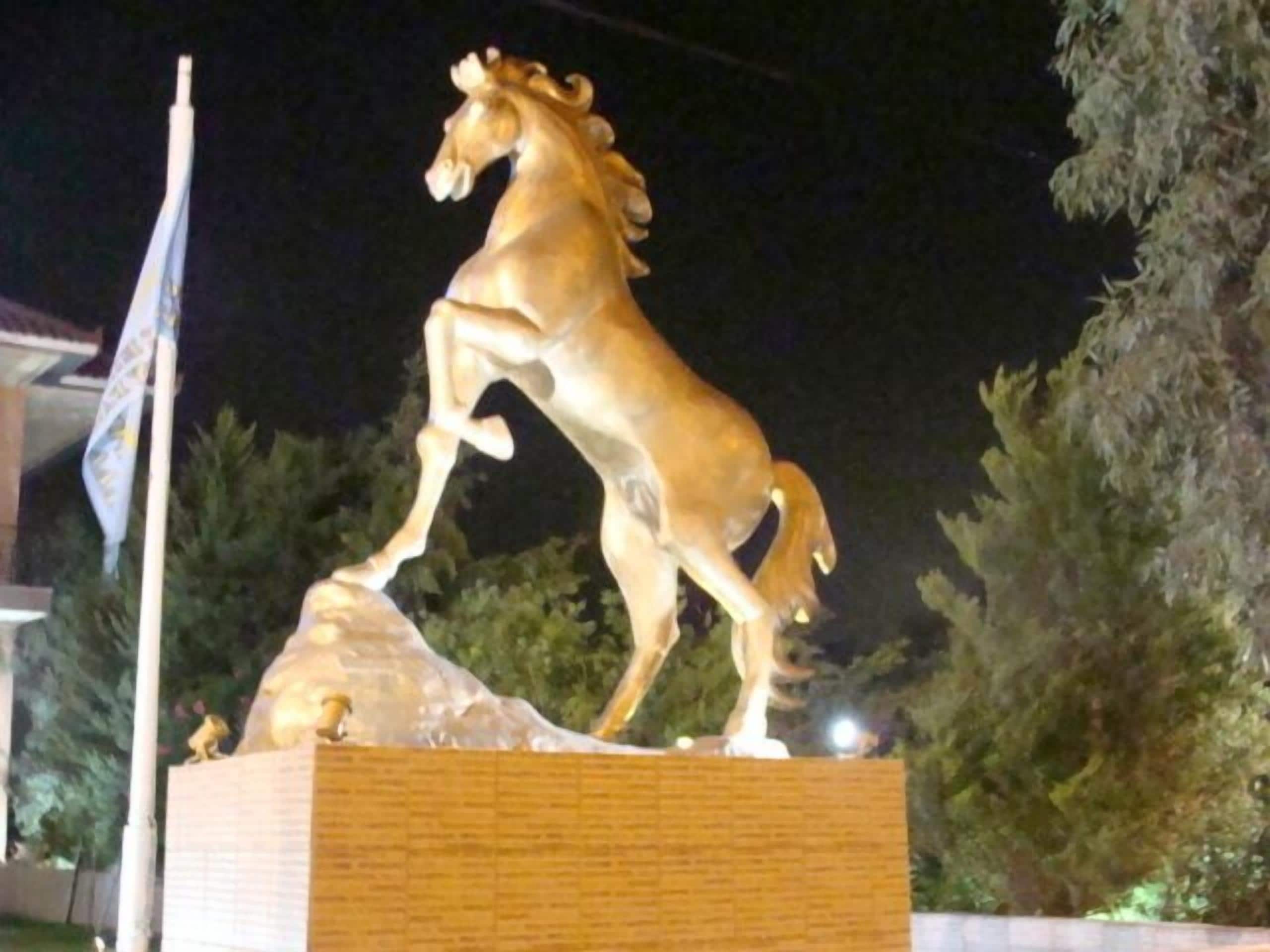 Una statua dorata di un cavallo su un piedistallo, con un'asta di bandiera a sinistra.