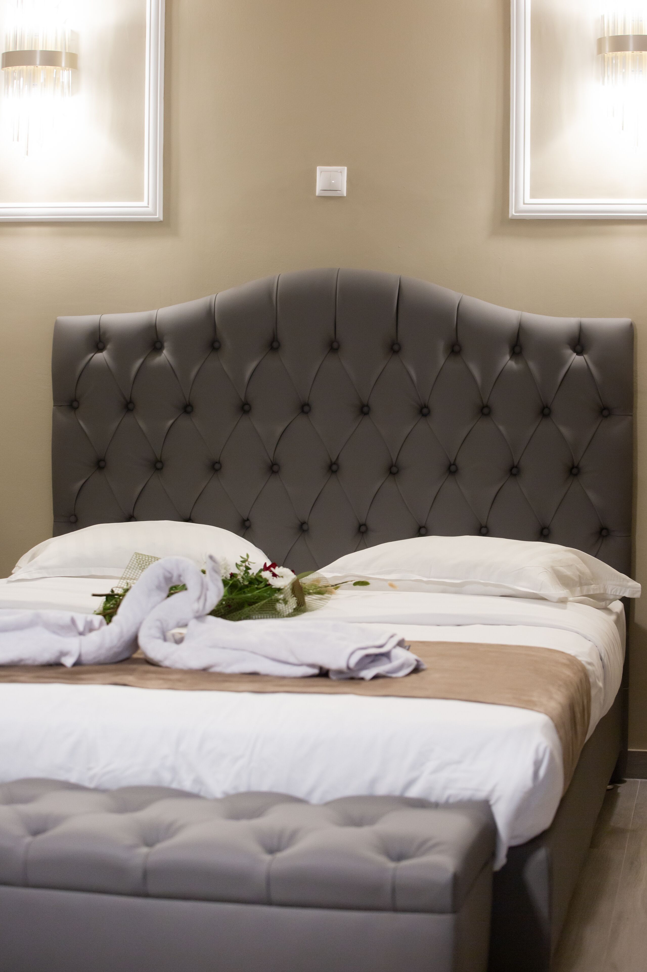 A neatly made bed with a tufted headboard, white linens, and a bouquet of flowers.