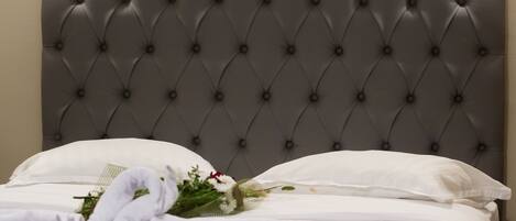 A neatly made bed with a tufted headboard, white linens, and a bouquet of flowers.