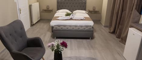 A bedroom with a bed, two armchairs, a small table with a vase, and a ceiling light.