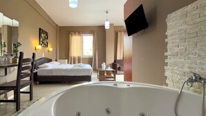 Habitación de hotel con una bañera grande, una cama, un escritorio con una silla, un televisor montado en la pared y una ventana con cortinas.