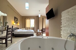 A hotel room with a large bathtub, a bed, a desk with a chair, a TV mounted on the wall, and a window with curtains. - Cavallari Palace Hotel (Acharnes)