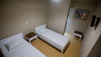 Una habitación con dos camas individuales, una mesita con una planta y un cuadro en la pared.