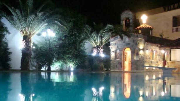 Vista nocturna de una piscina con palmeras y un edificio con una cúpula iluminada y una entrada en arco.