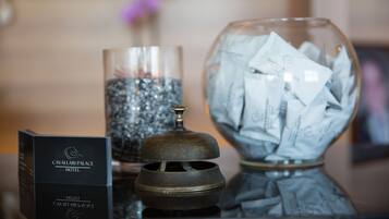 Uma área de recepção de hotel com uma placa preta, um recipiente de vidro com tampa e uma tigela cheia de papéis.