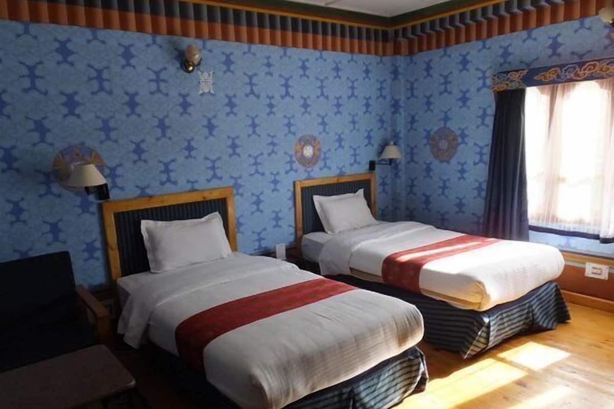 Hotellihuone, jossa on kaksi sänkyä, työpöytä ja ikkuna, jossa on verhot.