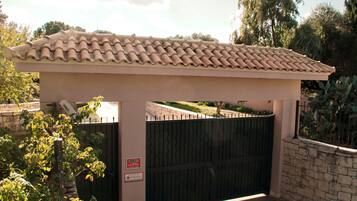 A gated entrance with a tiled roof, a metal gate, and a stone wall.