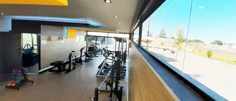 Un gimnasio con diversos equipos de ejercicio, ventanas amplias y vistas al exterior.