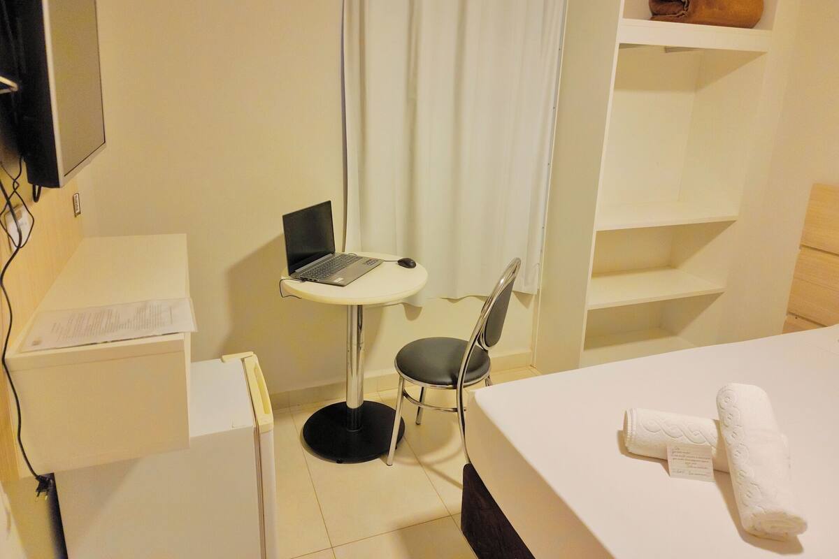 Habitación de hotel con escritorio, una computadora portátil, una silla, una cama y un estante con toallas.