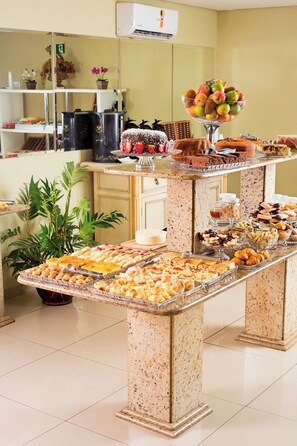 A buffet setup with various food items and a decorative plant. - WR Confort Hotel Campo Grande (Campo Grande)