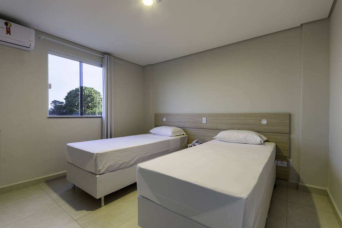 Una habitación de hotel con dos camas individuales, una ventana y un aire acondicionado instalado en la pared.