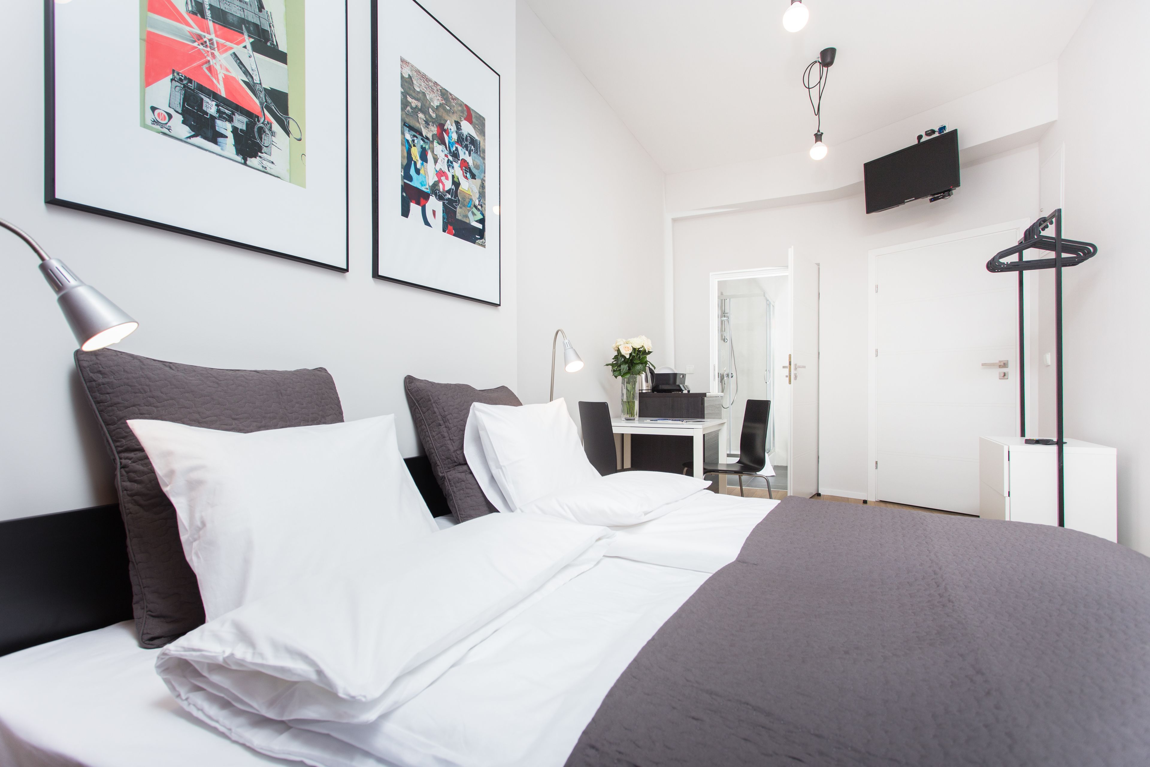 Habitación de hotel moderna con una cama grande, un escritorio, un espejo y un televisor montado en la pared.