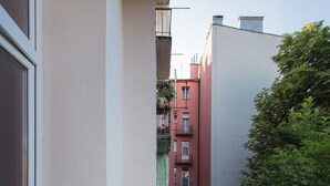 Un balcón estrecho con barandilla metálica, puerta de cristal y vista a edificios vecinos.