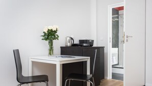 Una cocina pequeña y moderna con una mesa blanca y dos sillas negras, un florero con flores blancas y un armario negro.