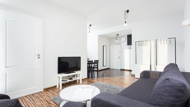 Una sala de estar moderna con un sofá gris, una mesa de centro blanca, un televisor de pantalla plana y piso de madera.