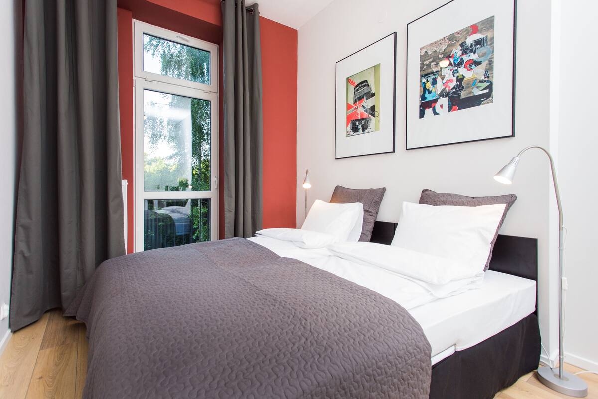 Un dormitorio moderno con una cama grande, una ventana con cortinas y dos cuadros en la pared.