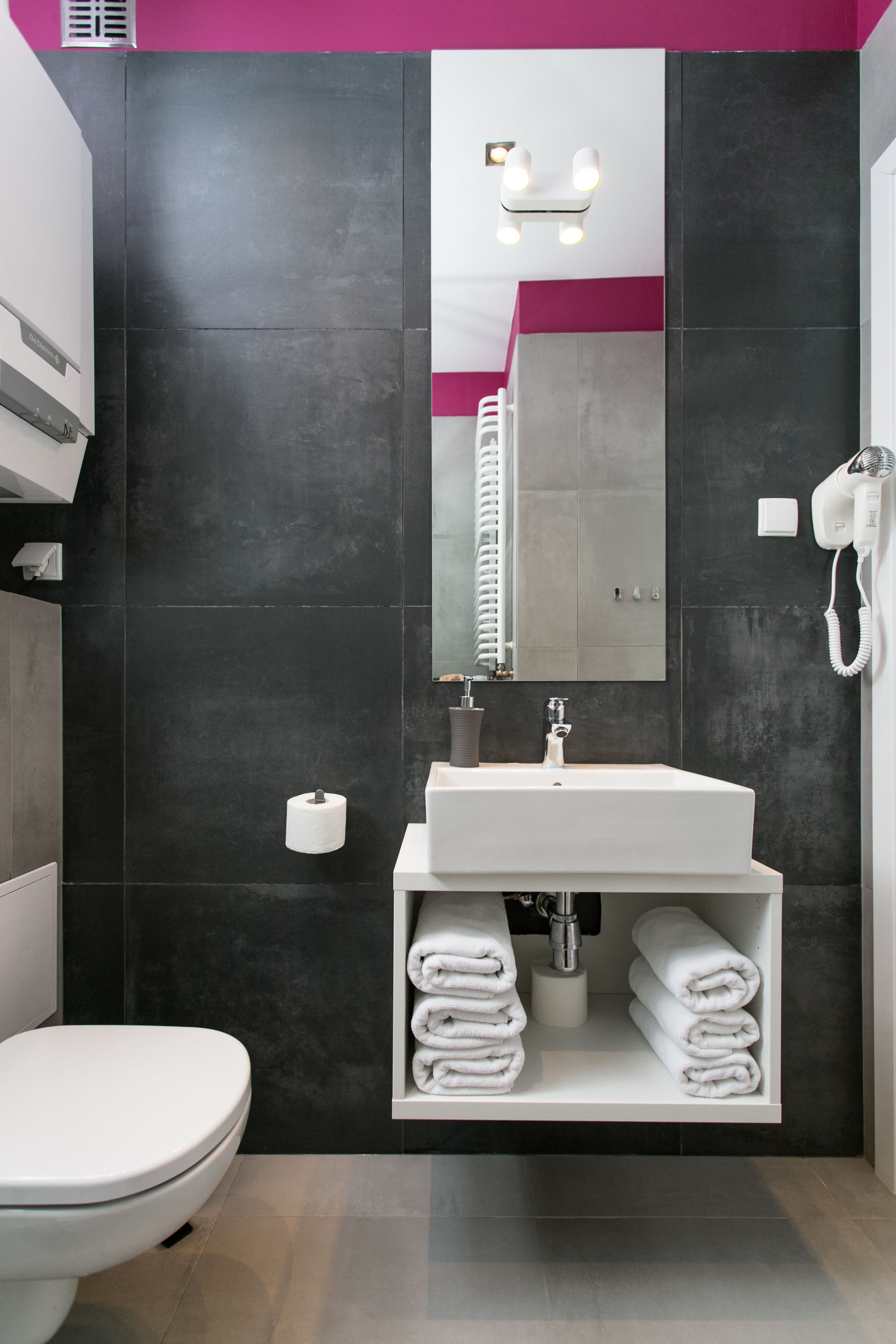 Une salle de bain moderne avec un lavabo blanc, un miroir, un sèche-cheveux et des toilettes.