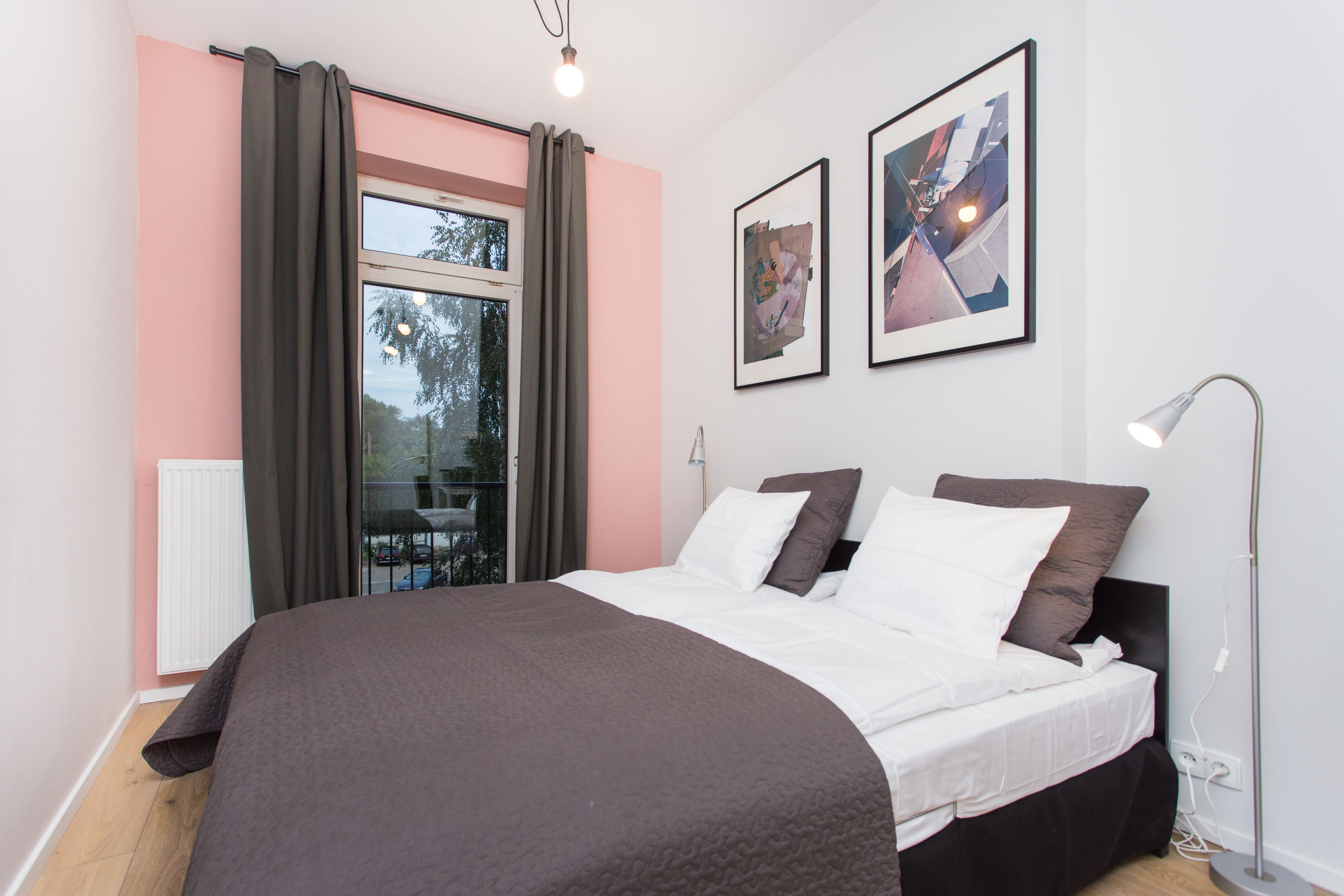 A bedroom with a large bed, a window with curtains, a radiator, and two framed pictures on the wall.