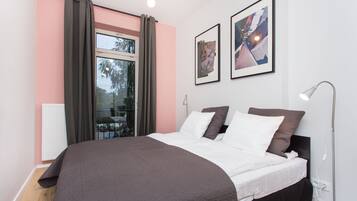 A bedroom with a large bed, a window with curtains, a radiator, and two framed pictures on the wall.