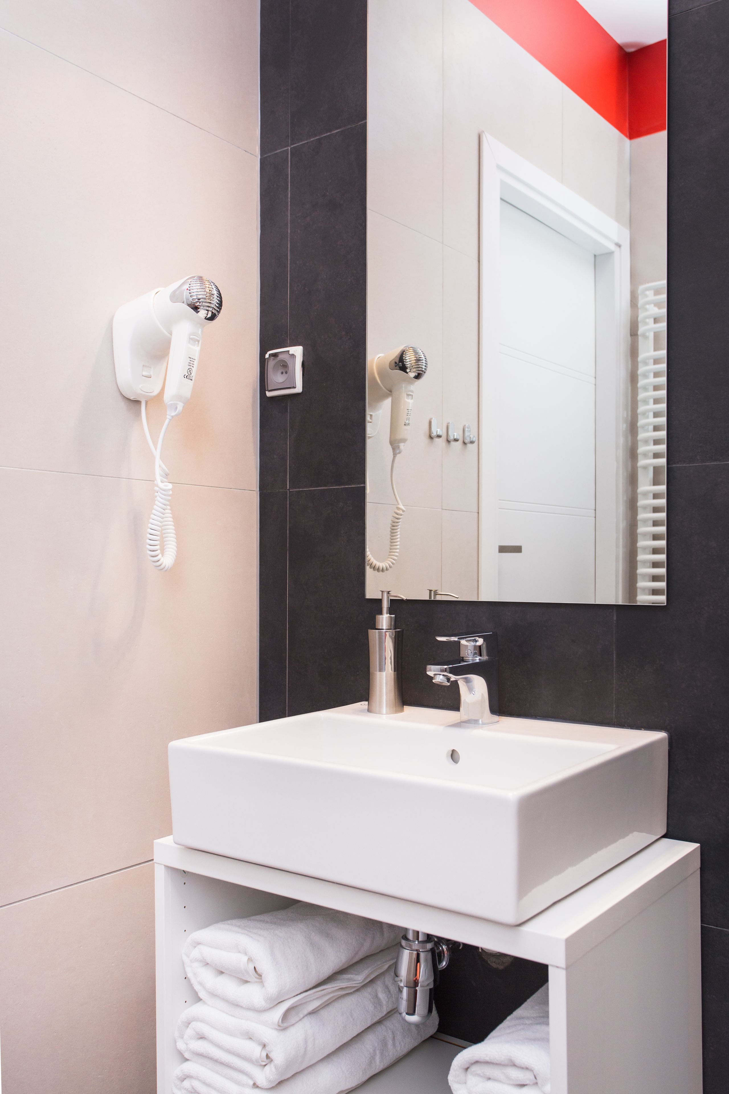 Un baño moderno con un lavamanos blanco, un espejo y dos secadores de pelo montados en la pared.
