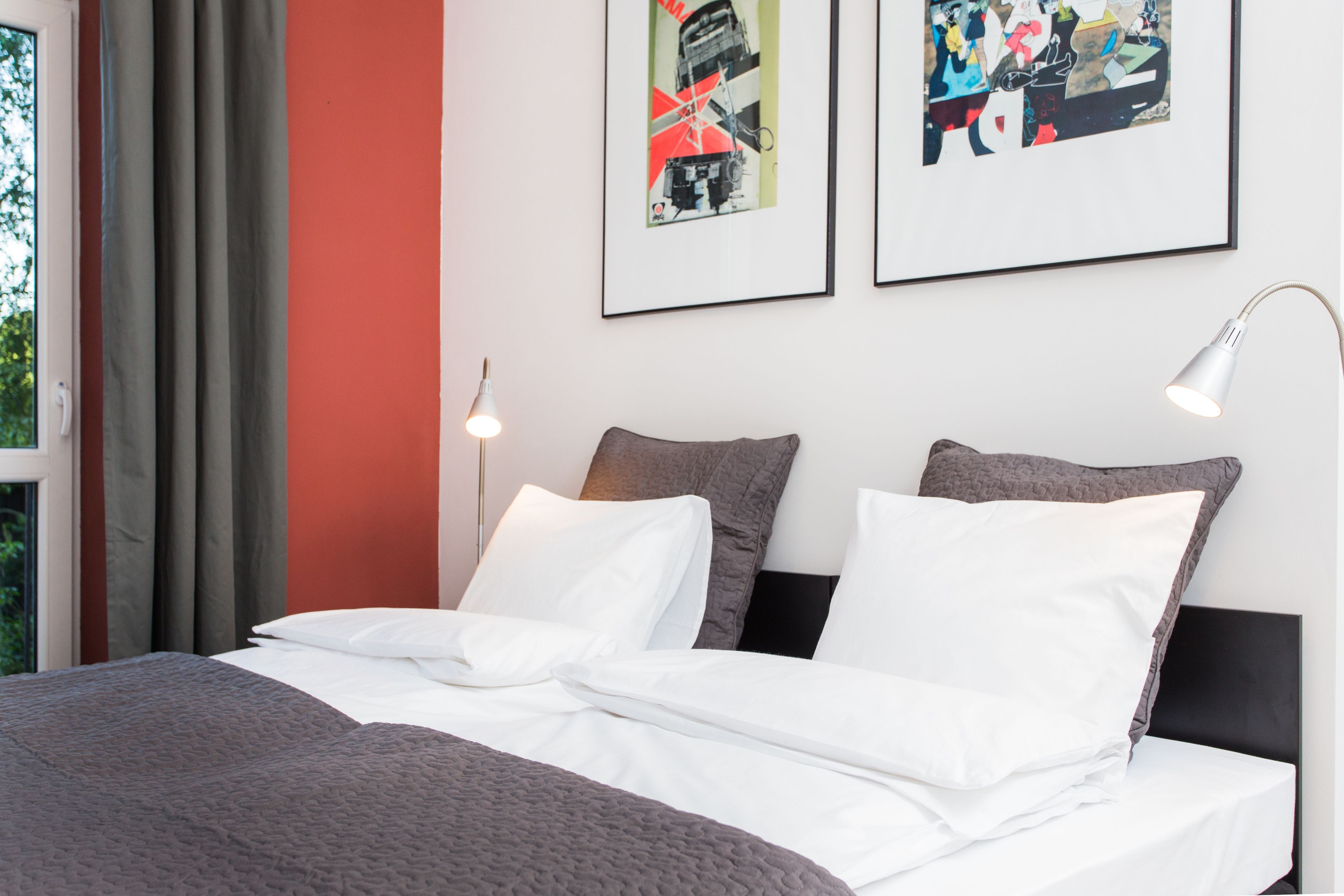 A neatly made bed with white and gray bedding, a gray blanket, and two pillows. There are two framed artworks on the wall above the bed.