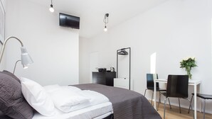 Un dormitorio moderno con cama, lámpara de noche, escritorio, silla y televisor en la pared.