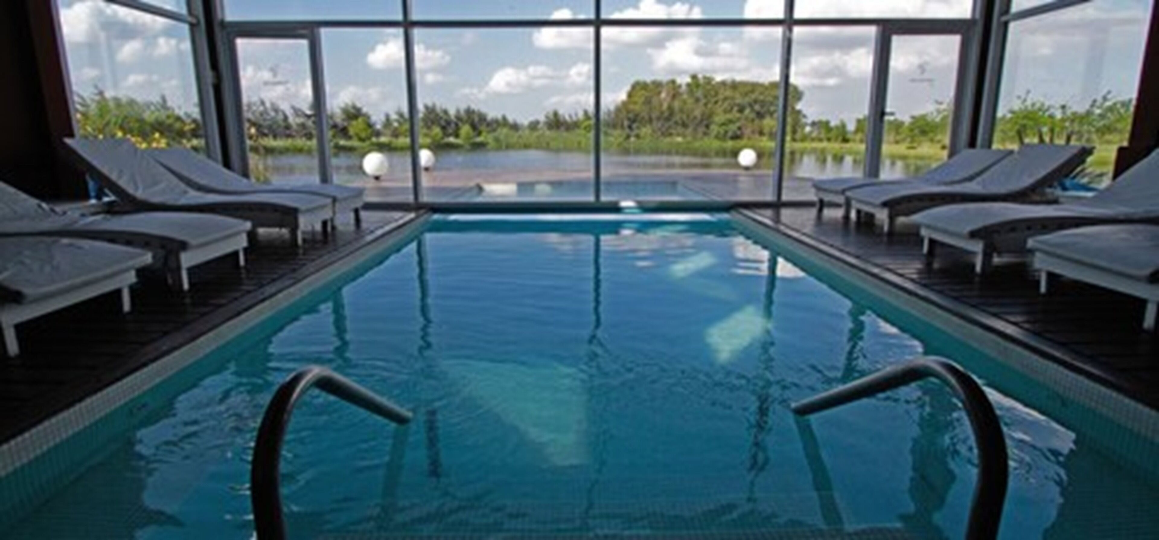 Una piscina interior con vistas despejadas al exterior, rodeada de sillones de descanso.