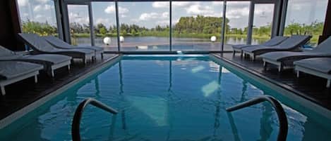An indoor swimming pool with clear views of the outdoors, surrounded by lounge chairs.