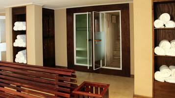 Quarto com um banco de madeira, guarda-roupa com toalhas e porta de armário com espelho.