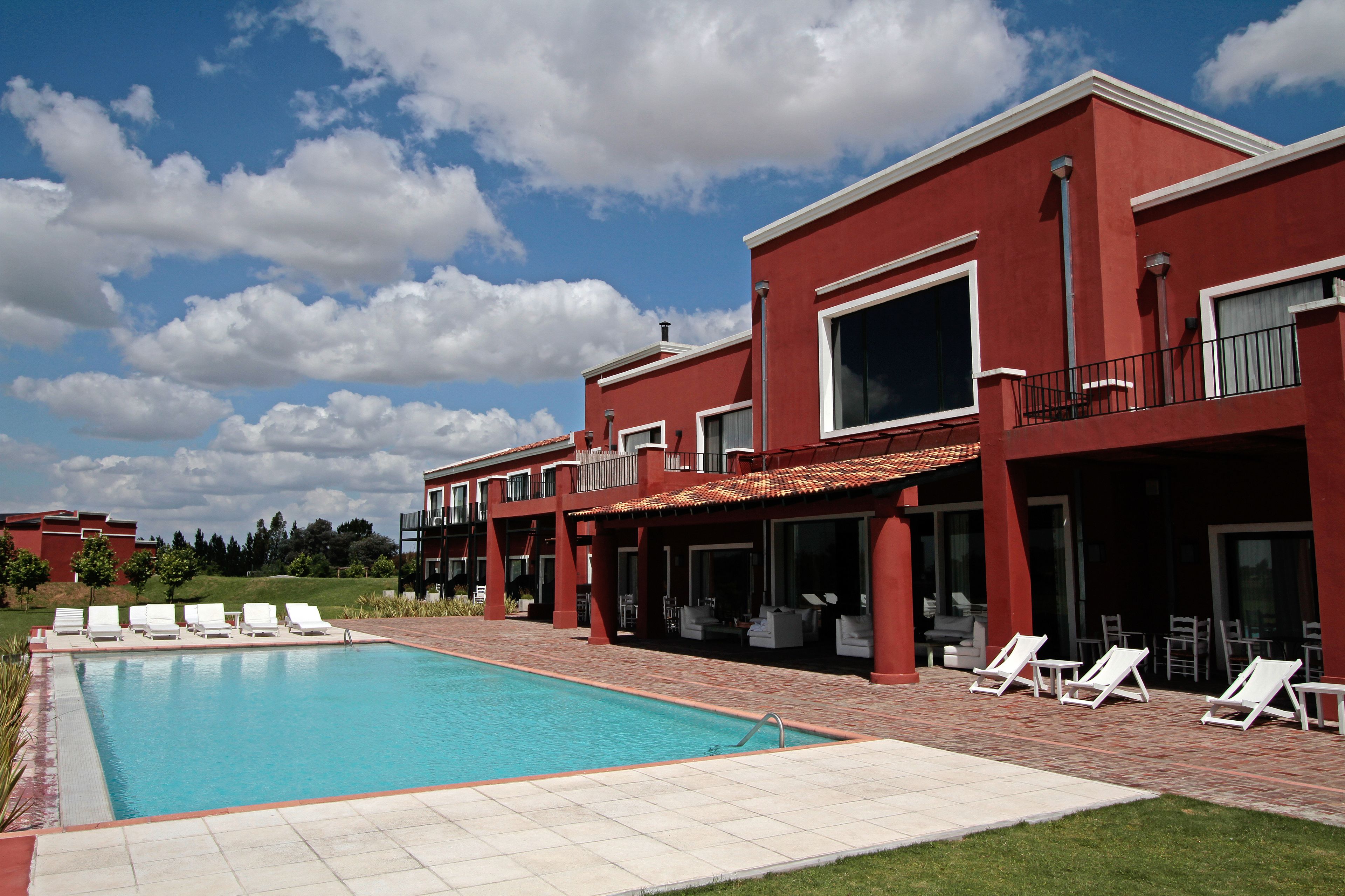 A modern building with a swimming pool, outdoor seating, and a clear blue sky.