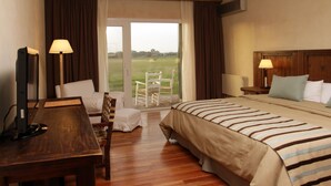 Quarto de hotel com uma cama grande, uma escrivaninha, uma cadeira, uma mesa de cabeceira e vista para o exterior.