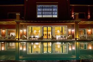 Un hotel con piscina, mobiliario exterior y una entrada amplia con puertas de cristal.