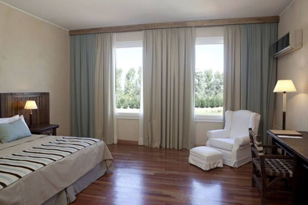 Una habitación de hotel con una cama, una silla, un escritorio y un ventanal con cortinas.