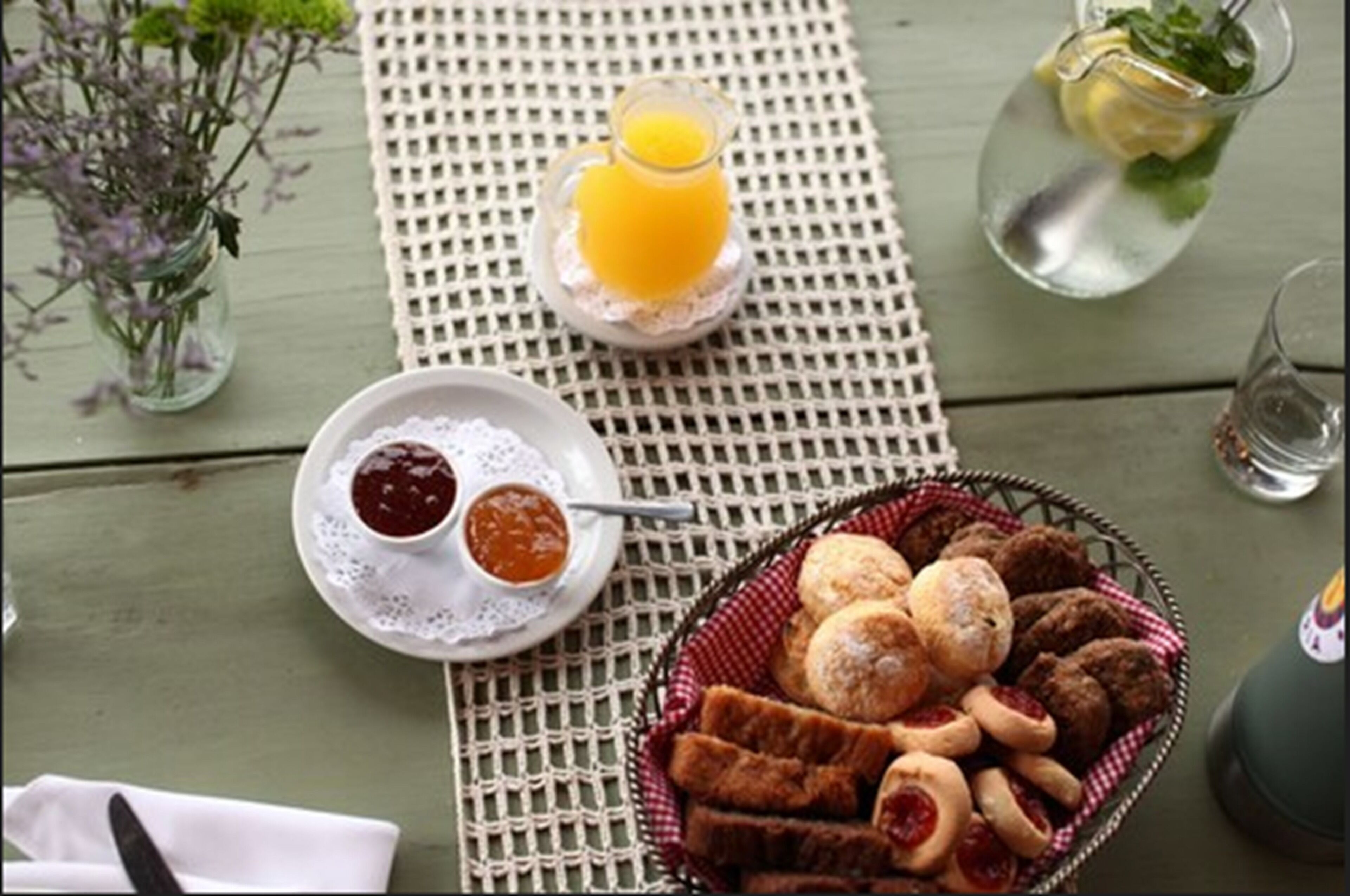 A table set with a basket of pastries, a glass of orange juice, and a small bowl of jam.