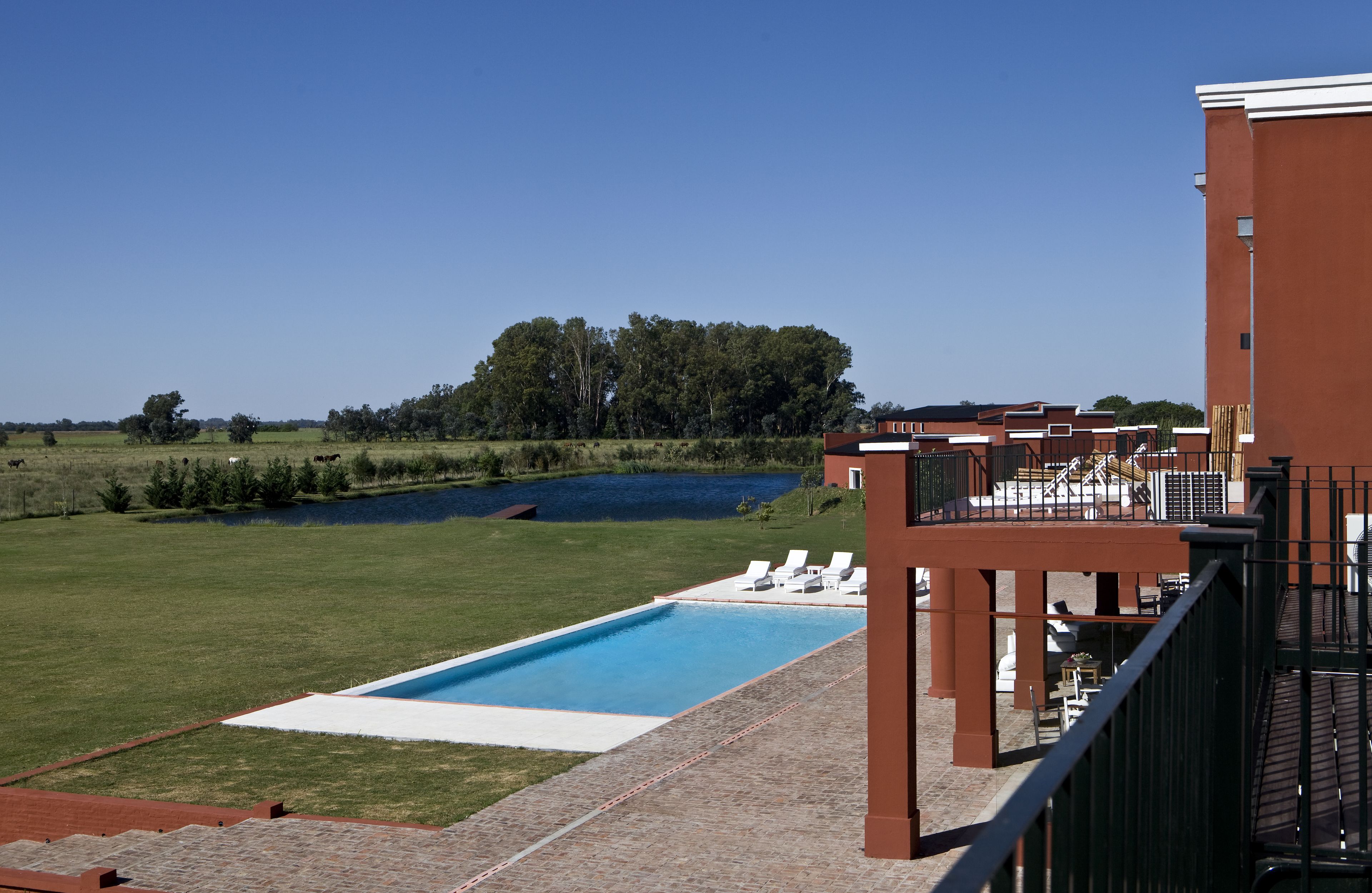 A swimming pool with lounge chairs, a grassy area, and a building with a red facade.