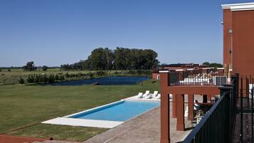 A swimming pool with lounge chairs, a grassy area, and a building with a red facade.