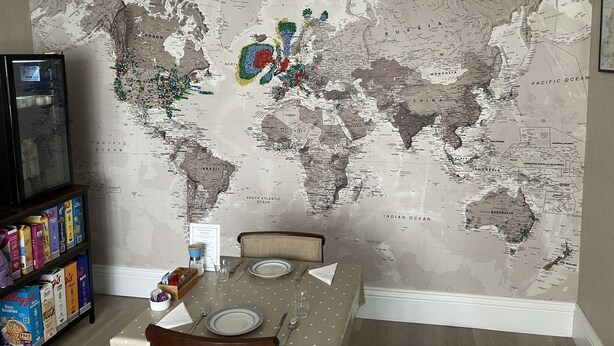 A dining area with a world map mural, a refrigerator, and a cereal box shelf. - Anvershiel House (Portrush)