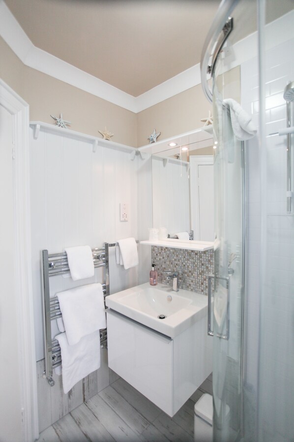 A modern bathroom with a glass shower enclosure, a white sink, and a towel rack.