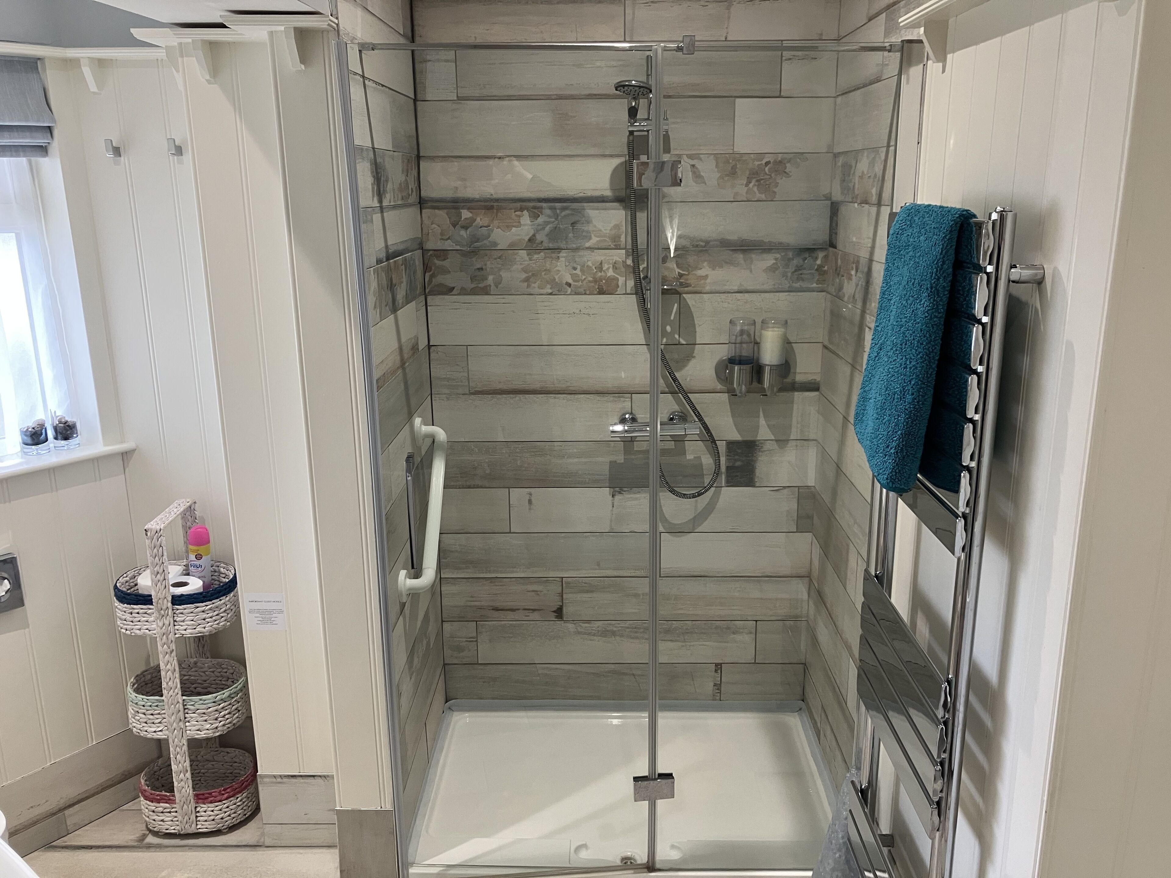 A modern bathroom with a glass-enclosed shower, a white bathtub, and a towel rack with a blue towel.