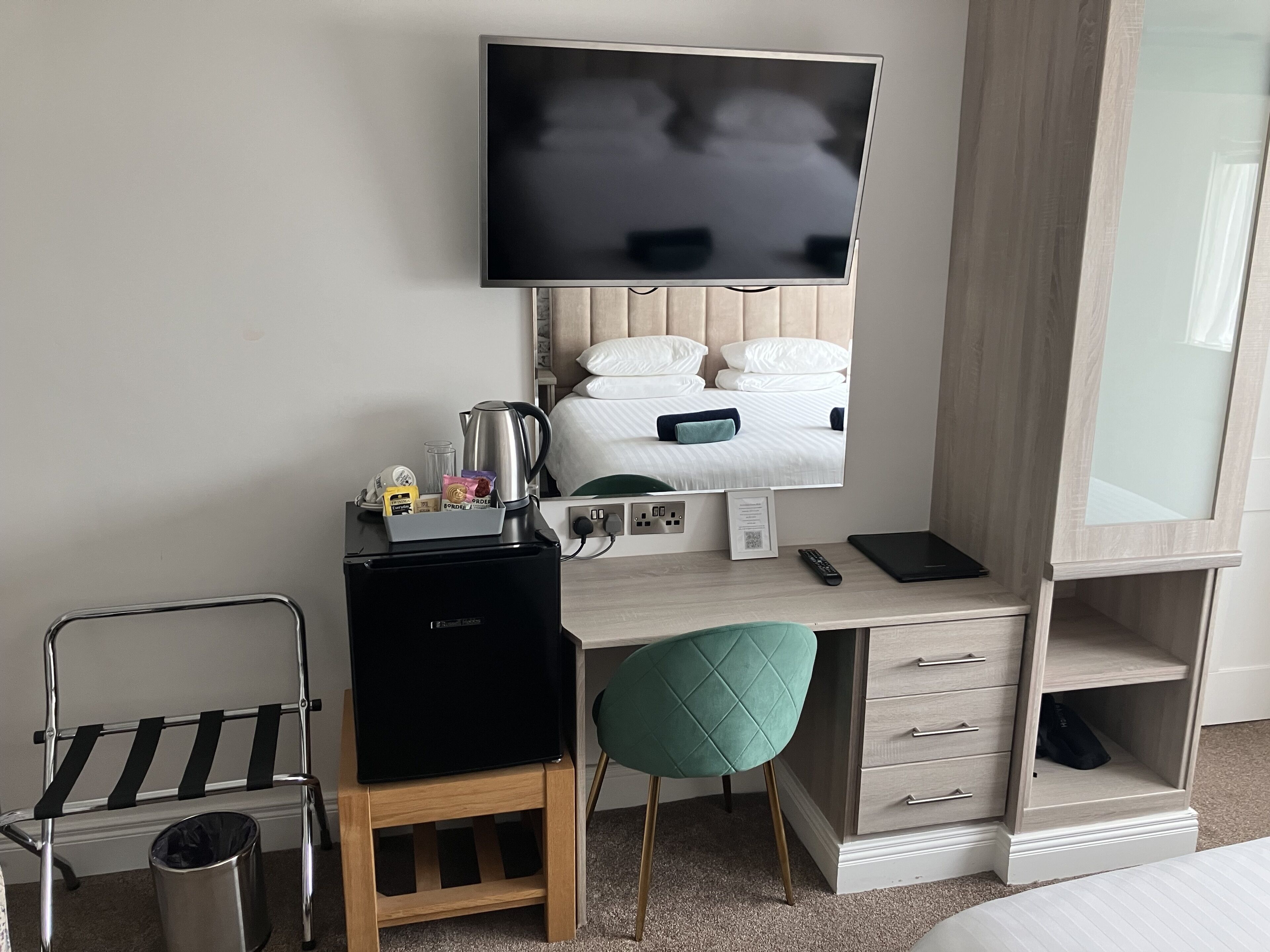 Une chambre d’hôtel équipée d’un lit, d’un bureau, d’une télévision, d’une bouilloire, d’une poubelle et d’une chaise.