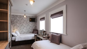A bedroom with two beds, a desk, a television, and a brick-patterned wall. - Anvershiel House (Portrush)